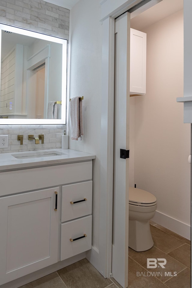bathroom with tile patterned floors, toilet, vanity, baseboards, and backsplash