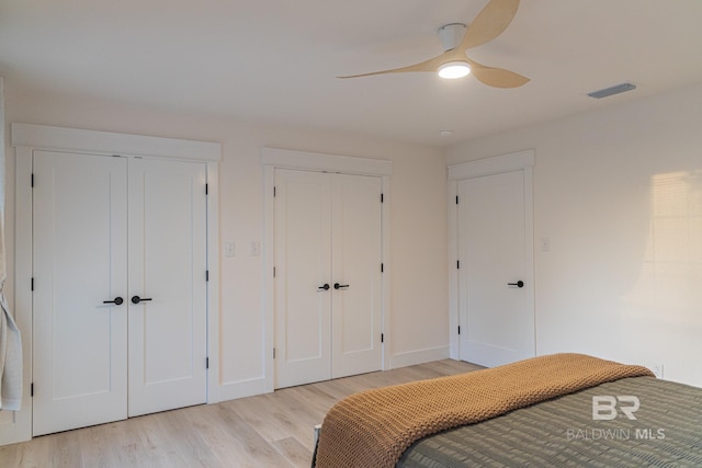 bedroom featuring two closets, light wood-type flooring, baseboards, and ceiling fan