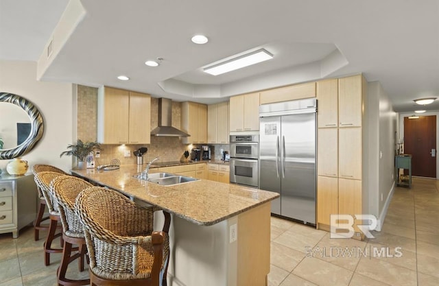 kitchen featuring light stone counters, appliances with stainless steel finishes, wall chimney range hood, and kitchen peninsula