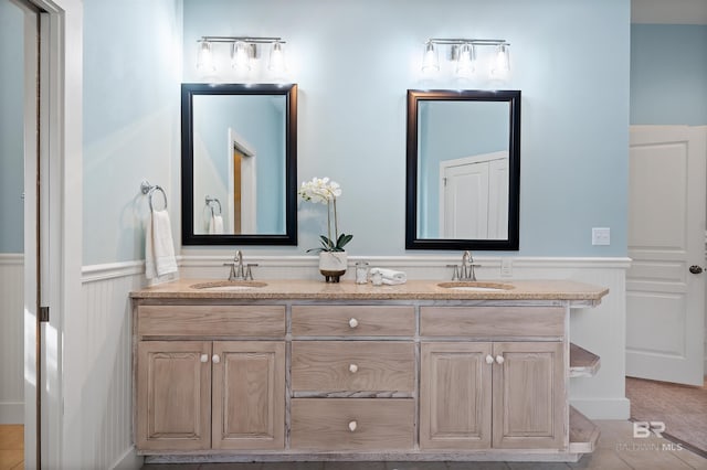 full bath featuring double vanity, a wainscoted wall, and a sink