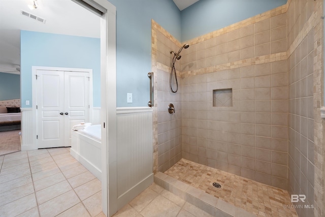 bathroom with tile patterned flooring, wainscoting, a tile shower, and visible vents