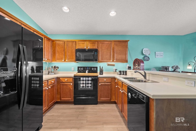 kitchen featuring black appliances, brown cabinetry, a peninsula, and a sink