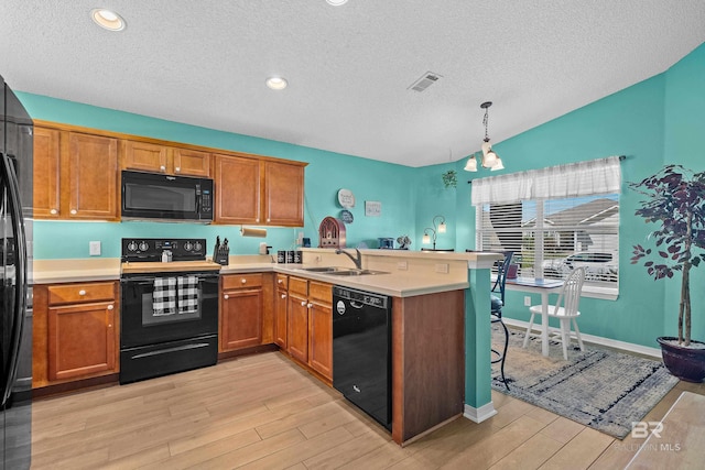 kitchen with black appliances, brown cabinetry, a peninsula, and a sink