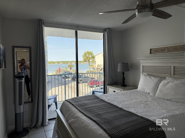 bedroom featuring a water view, expansive windows, light tile patterned floors, a textured ceiling, and access to outside