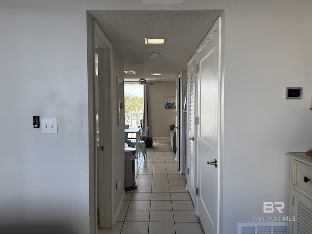 hall featuring light tile patterned floors, baseboards, visible vents, and a textured ceiling