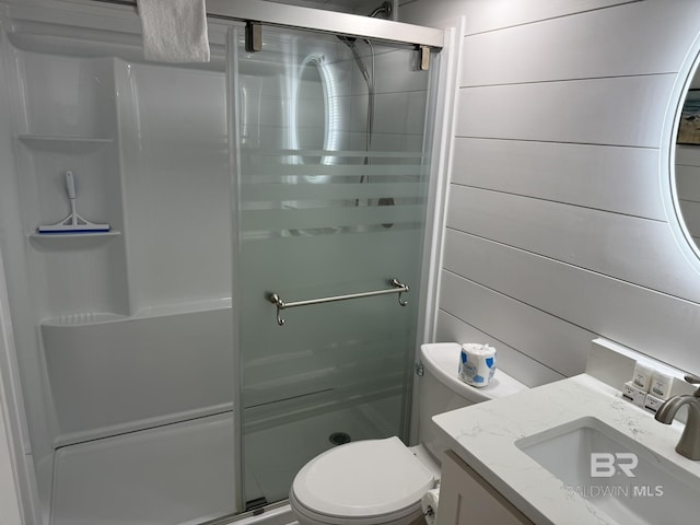 full bathroom featuring vanity, wooden walls, a shower stall, and toilet