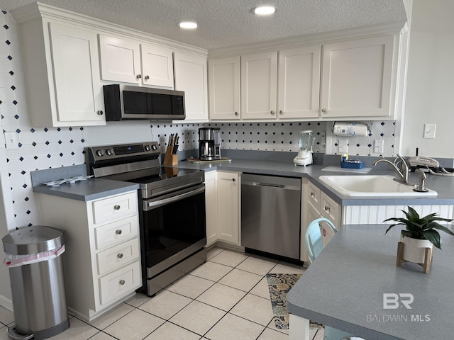 kitchen featuring light tile patterned flooring, a sink, appliances with stainless steel finishes, a textured ceiling, and white cabinetry