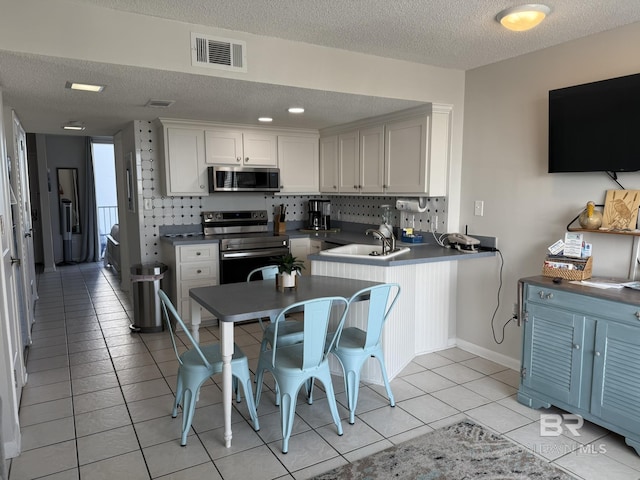 kitchen with visible vents, a sink, backsplash, stainless steel appliances, and light tile patterned floors