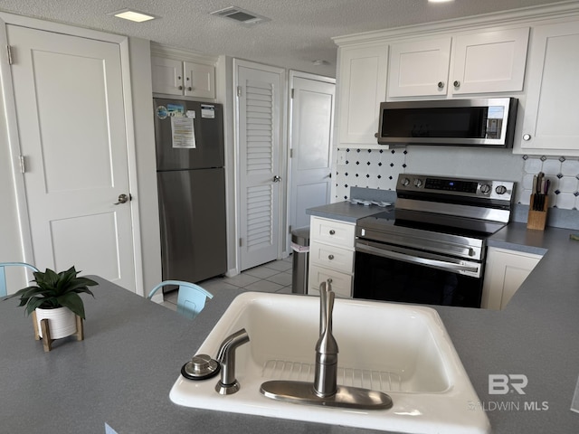 kitchen with visible vents, light tile patterned floors, stainless steel appliances, a textured ceiling, and white cabinetry