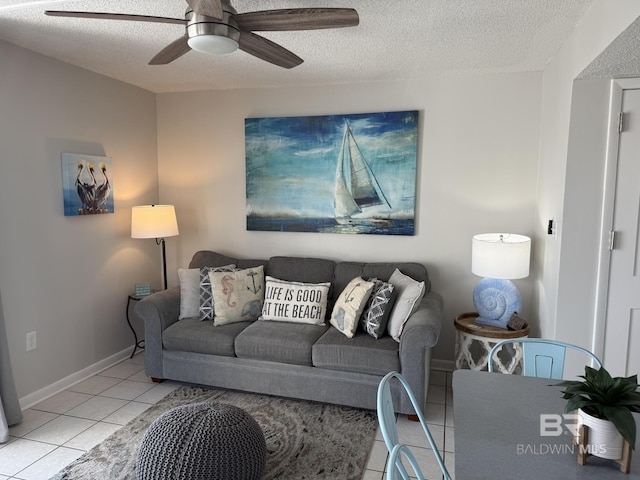 living area featuring light tile patterned flooring, baseboards, a textured ceiling, and ceiling fan