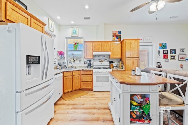 kitchen featuring a breakfast bar area, under cabinet range hood, white appliances, a sink, and visible vents