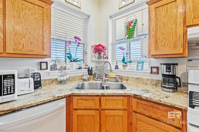 kitchen featuring light stone countertops, white appliances, and a sink