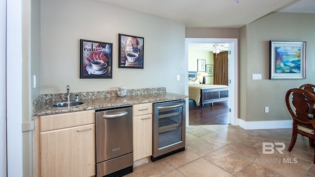 kitchen with wine cooler, a sink, dishwasher, light brown cabinetry, and light stone counters