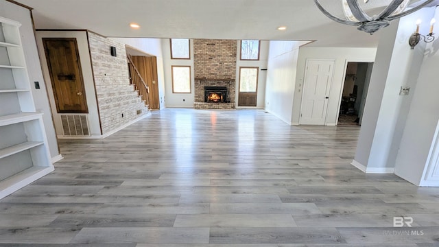 unfurnished living room featuring built in shelves, light hardwood / wood-style floors, a fireplace, and an inviting chandelier