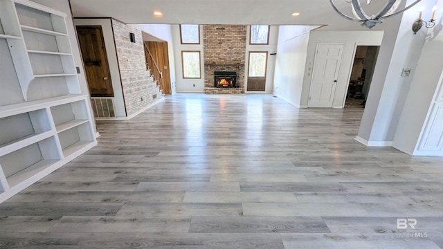 unfurnished living room featuring a chandelier, a brick fireplace, light wood-type flooring, and built in features