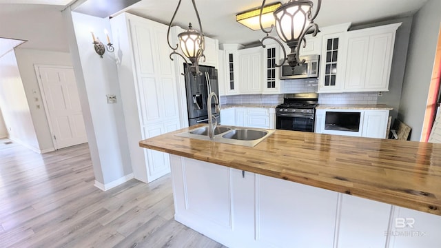 kitchen with wooden counters, appliances with stainless steel finishes, sink, white cabinets, and hanging light fixtures