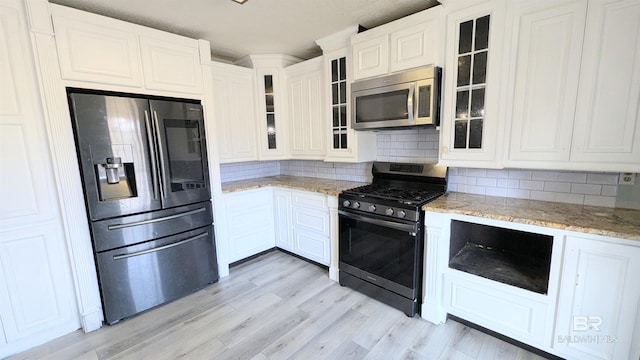 kitchen with appliances with stainless steel finishes, backsplash, white cabinetry, and light stone counters