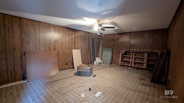 interior space featuring ceiling fan, wooden walls, and a textured ceiling