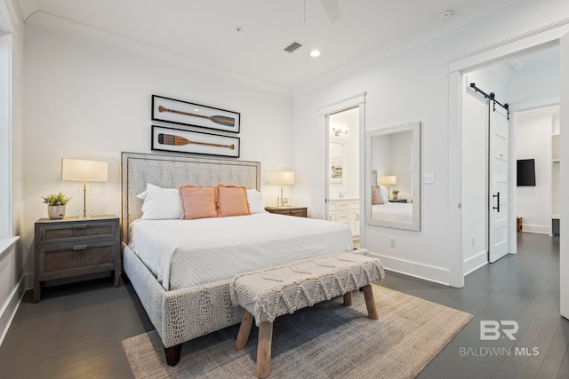 bedroom featuring ornamental molding, a barn door, dark hardwood / wood-style flooring, and ensuite bath