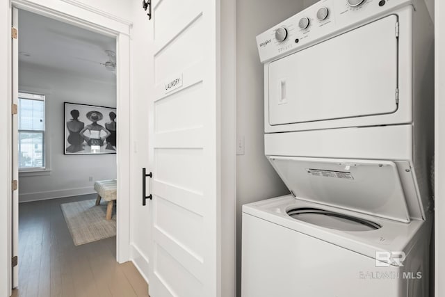 laundry area featuring stacked washer / drying machine, wood-type flooring, and a barn door