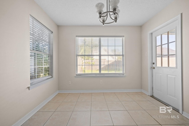 unfurnished dining area featuring plenty of natural light, light tile patterned flooring, a textured ceiling, and an inviting chandelier