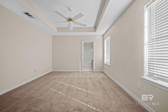 unfurnished room featuring light carpet, a textured ceiling, a tray ceiling, and ceiling fan