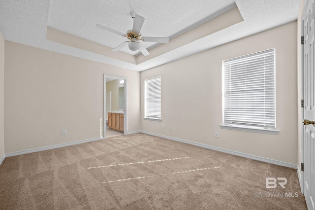 unfurnished bedroom featuring ensuite bathroom, a raised ceiling, ceiling fan, a textured ceiling, and light colored carpet