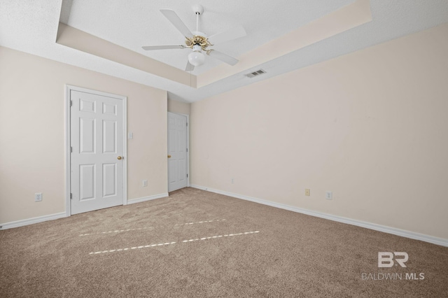 unfurnished bedroom with a tray ceiling, ceiling fan, and carpet floors