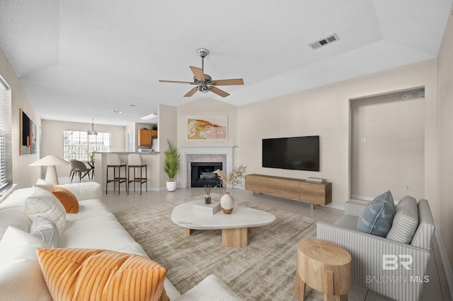 tiled living room featuring a raised ceiling, a tile fireplace, ceiling fan, and vaulted ceiling