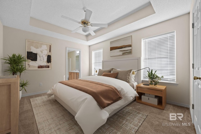 bedroom featuring multiple windows, connected bathroom, a raised ceiling, and ceiling fan