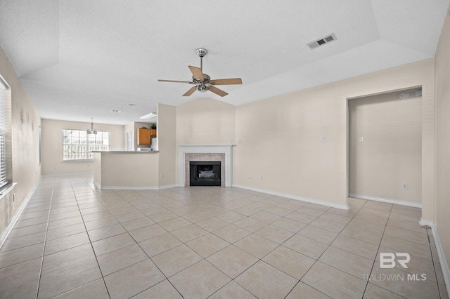 unfurnished living room with a tile fireplace, light tile patterned floors, ceiling fan with notable chandelier, and a raised ceiling