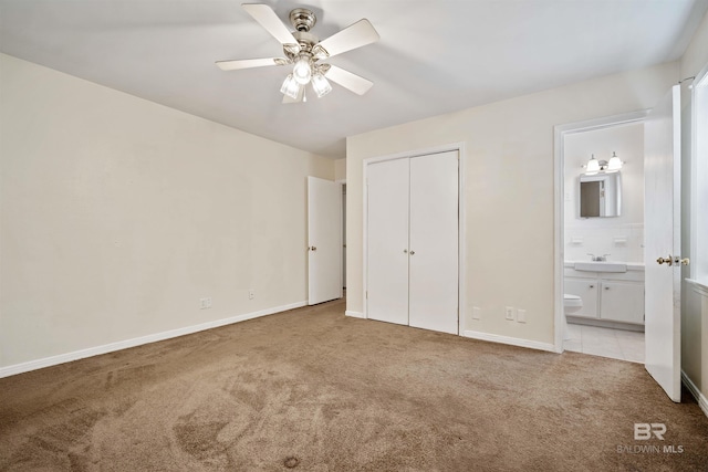 unfurnished bedroom featuring sink, ensuite bath, ceiling fan, light colored carpet, and a closet