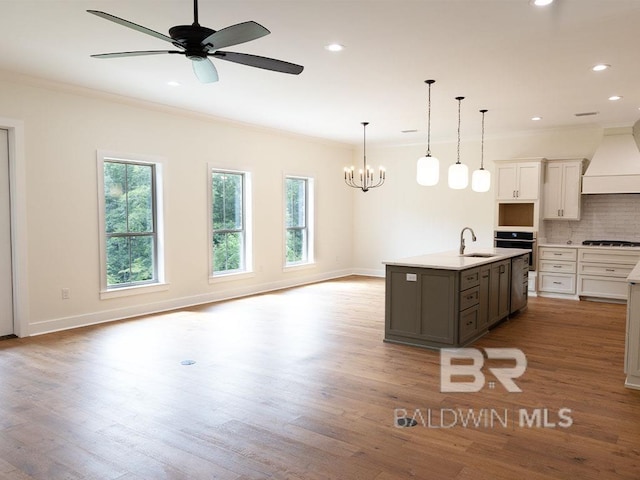 kitchen featuring backsplash, custom exhaust hood, sink, a center island with sink, and white cabinetry