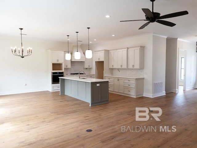 kitchen featuring a kitchen island with sink, oven, decorative light fixtures, and ornamental molding