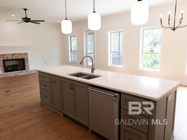 kitchen featuring sink, a brick fireplace, light stone counters, pendant lighting, and a center island with sink