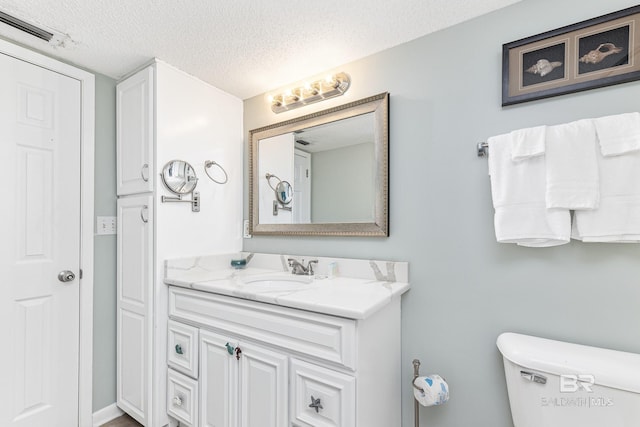 half bath with toilet, a textured ceiling, visible vents, and vanity