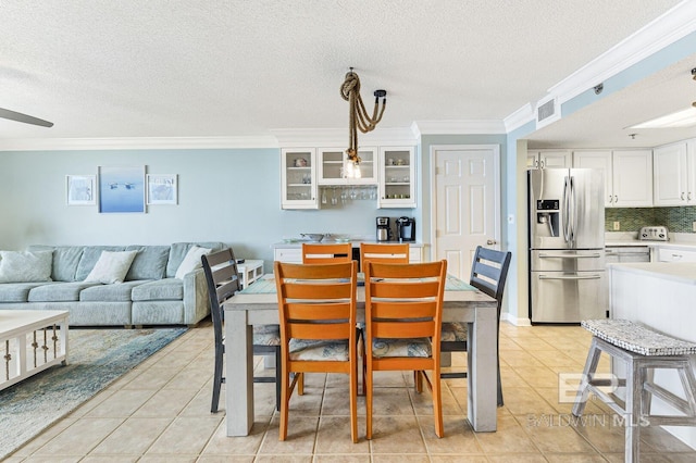 dining room with crown molding, a textured ceiling, light tile patterned flooring, and visible vents