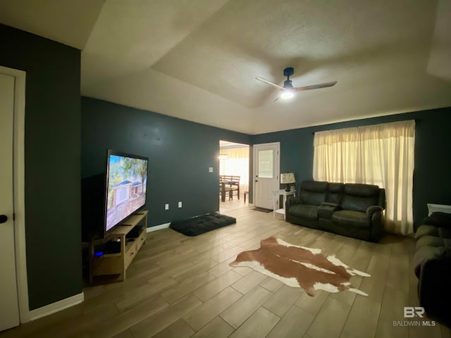 living room featuring a tray ceiling, ceiling fan, and light hardwood / wood-style floors