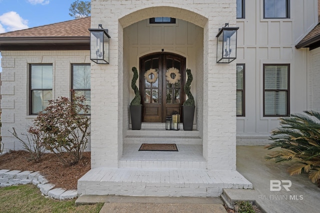 view of exterior entry featuring a shingled roof, board and batten siding, and brick siding