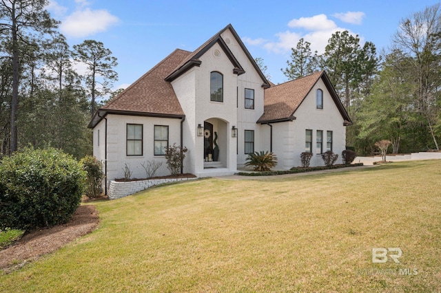 french provincial home featuring brick siding, roof with shingles, and a front lawn