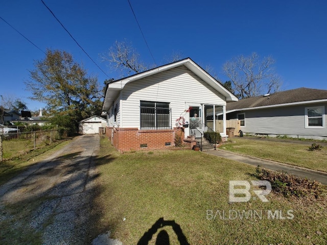 view of front of property featuring driveway, an outbuilding, crawl space, a front lawn, and brick siding