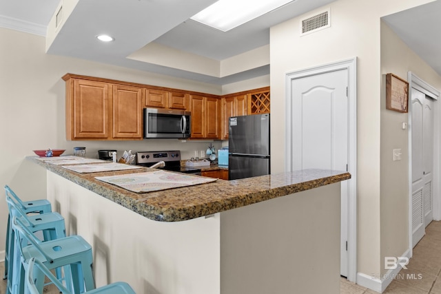 kitchen featuring kitchen peninsula, appliances with stainless steel finishes, dark stone countertops, a breakfast bar area, and light tile patterned flooring