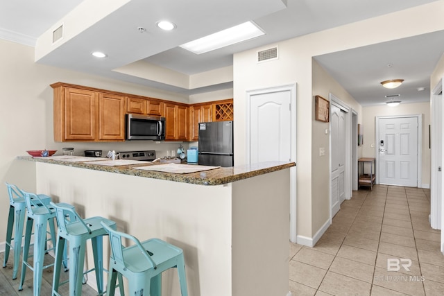 kitchen with kitchen peninsula, light tile patterned floors, stainless steel appliances, and a breakfast bar area