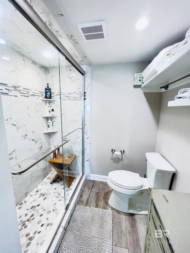 bathroom with toilet, a shower with door, and wood-type flooring