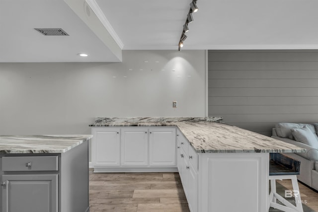 kitchen featuring light hardwood / wood-style flooring, light stone counters, white cabinets, a breakfast bar area, and ornamental molding