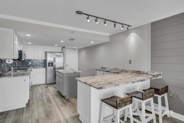 kitchen featuring appliances with stainless steel finishes, light hardwood / wood-style flooring, a kitchen island, white cabinets, and tasteful backsplash