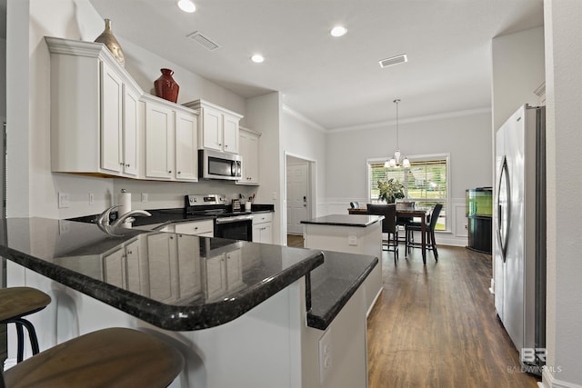 kitchen with appliances with stainless steel finishes, a center island, a peninsula, ornamental molding, and dark wood finished floors