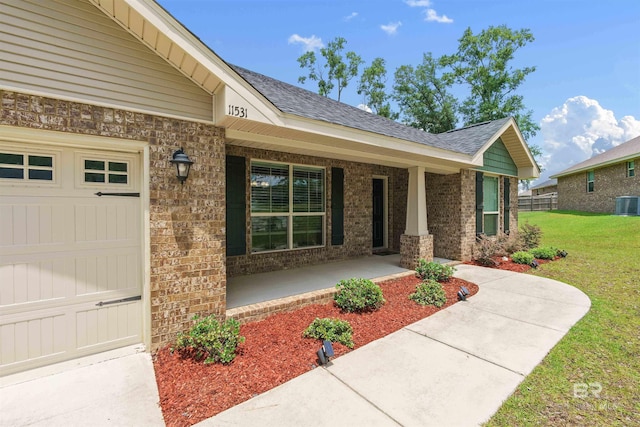 property entrance featuring covered porch, a lawn, brick siding, roof with shingles, and central AC