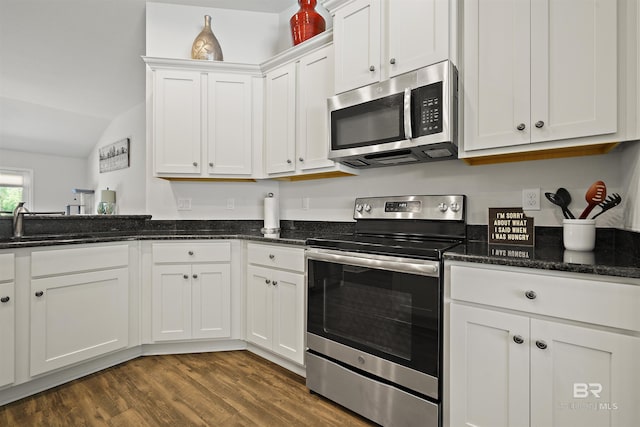 kitchen with stainless steel appliances, white cabinets, vaulted ceiling, dark wood-style flooring, and dark stone countertops