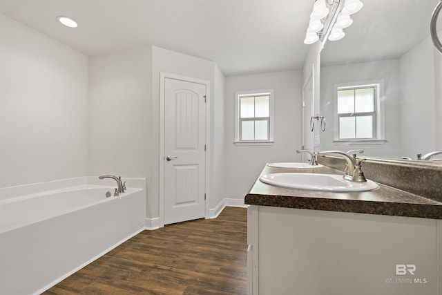 bathroom with wood finished floors, a garden tub, double vanity, and baseboards